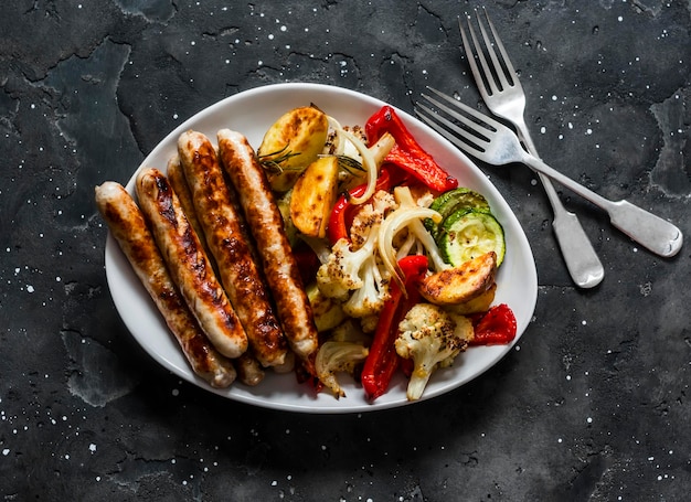 Grilled turkey sausages and roasted vegetables on a dark background top view Delicious lunch tapas appetizer