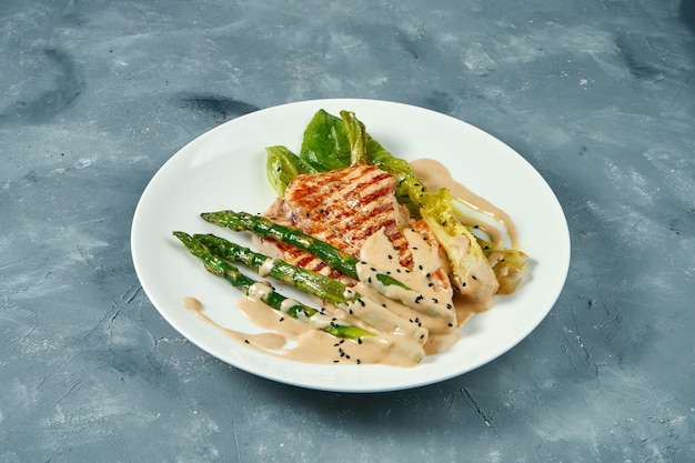 Grilled turkey steak with asparagus and sauce in white plate on gray surface