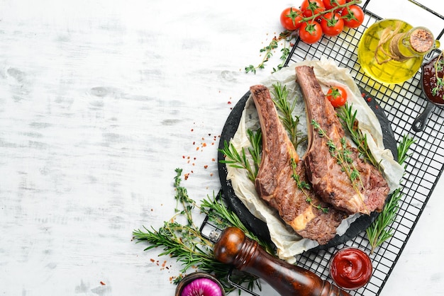 Grilled veal steak on the bone with spices and vegetables on a white wooden background Flat lay Top view