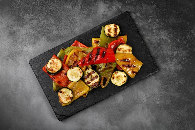 Grilled vegetable bell sweet pepper and zucchini on a black slate board and dark background