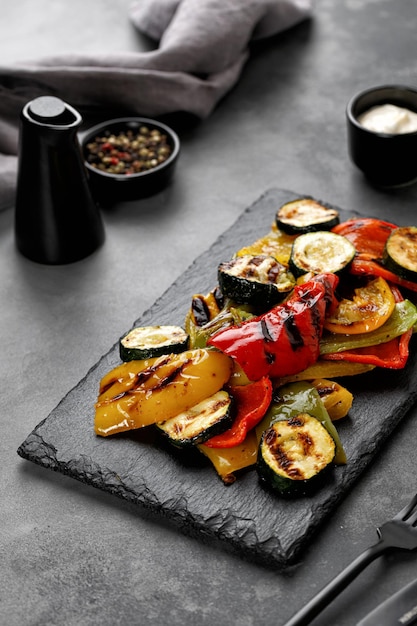 Жареный овощной сладкий перец и кабачки с соусом на темном фоне черной грифельной доски
