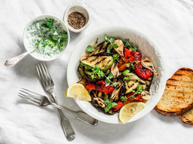 Grilled vegetables eggplant zucchini pepper salad with tzadziki Greek yogurt sauce on a light background top view Delicious appetizer tapas snack