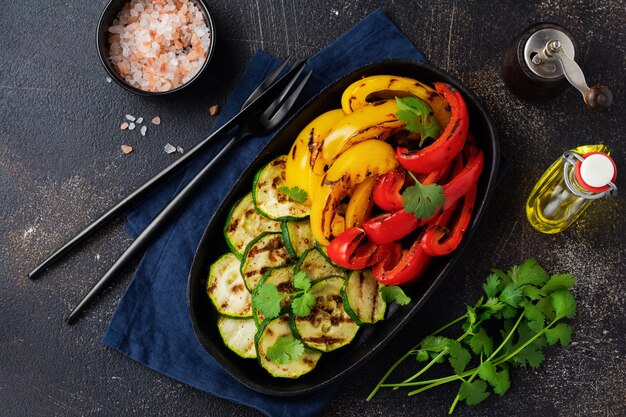 Grilled vegetables pieces of zucchini, red and yellow pepper and bouquet of cilantro on plate, salad on bbq grill rack over charcoal.  Barbecue concept.