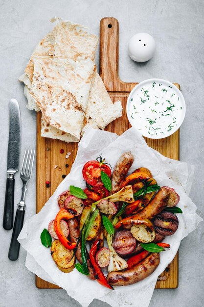 Grilled vegetables and sausages on wooden board top view