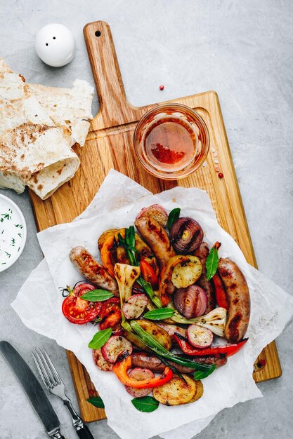 Grilled vegetables and sausages on wooden board top view