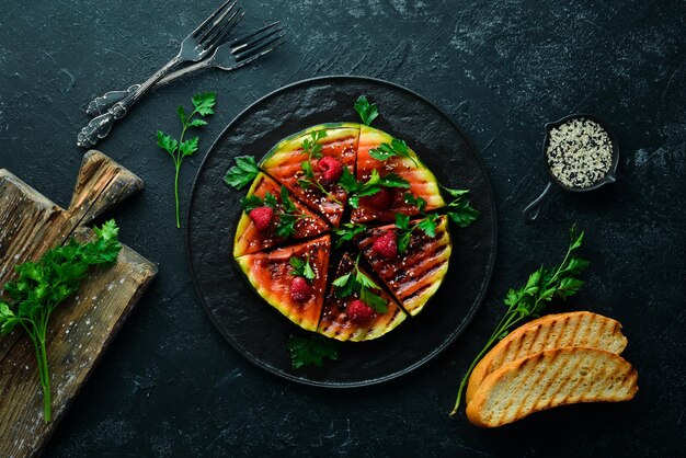 Grilled watermelon with raspberries and parsley on a black plate. Top view. Free copy space.