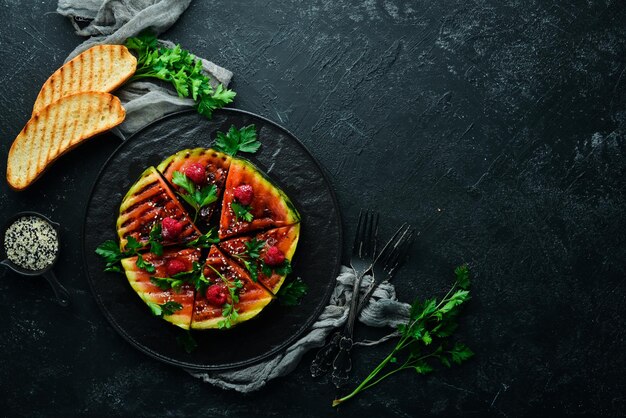 Grilled watermelon with raspberries and parsley on a black plate Top view Free copy space