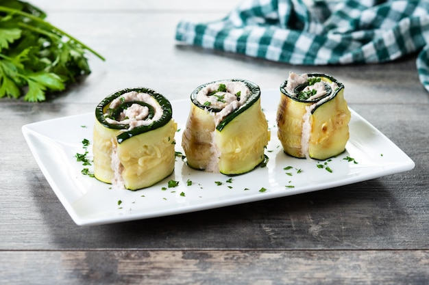 Grilled zucchini rolls stuffed with cream cheese and tuna on wooden table