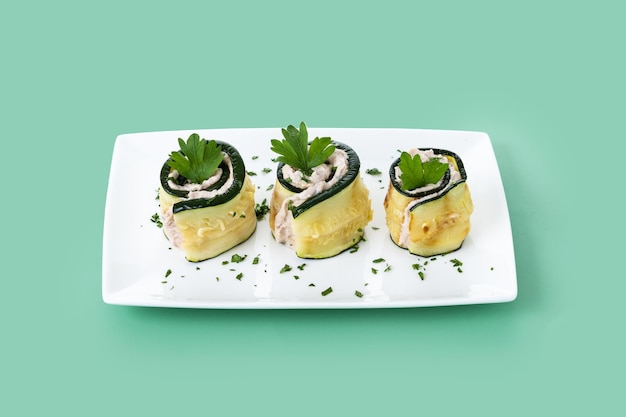 Grilled zucchini rolls with tuna and cream cheese on green background