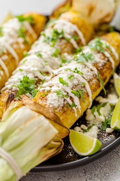 Grillen van Mexicaanse straatmaïs elote gegarneerd met kruiden en verse koriander op een serveerschaal.