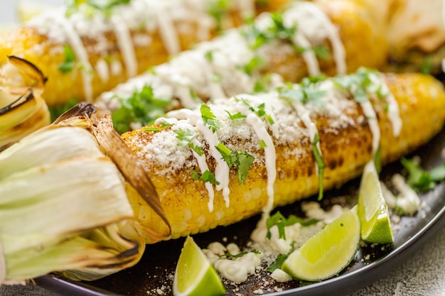 Grillen van Mexicaanse straatmaïs elote gegarneerd met kruiden en verse koriander op een serveerschaal.