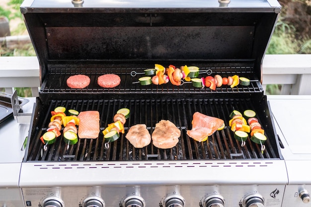 Grilling an Atlantic salmon, chicken breast, vegetable skewers, and vegetarian burgers on an outdoor grill.