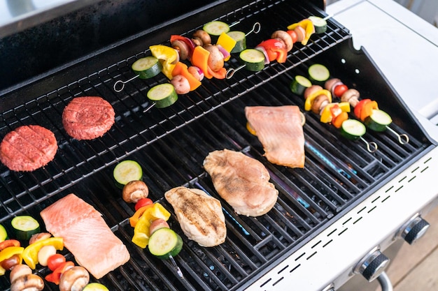 Grilling an Atlantic salmon, chicken breast, vegetable skewers, and vegetarian burgers on an outdoor grill.