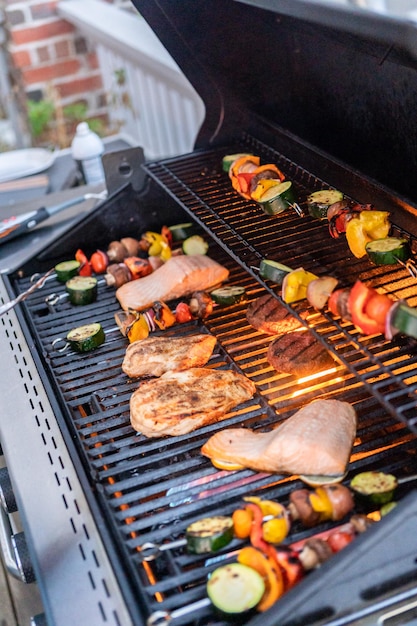 Grilling an Atlantic salmon, chicken breast, vegetable skewers, and vegetarian burgers on an outdoor grill.