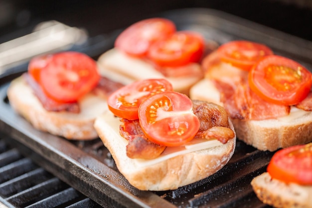 Grilling grilled cheese sandwich with bacon strips and fresh tomato on outdoor gas grill.