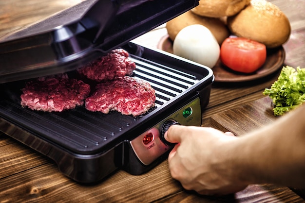 Grilling meat for hamburgers in an electric grill on a wooden table