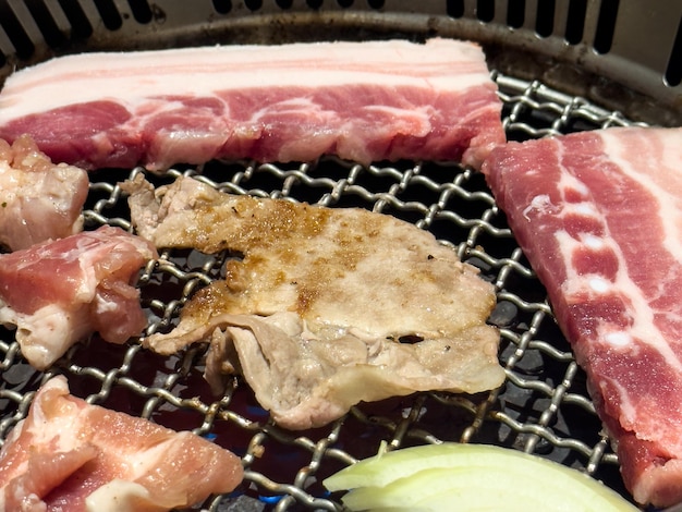 Grilling pork belly meat on a round BBQ net in restaurant for eating