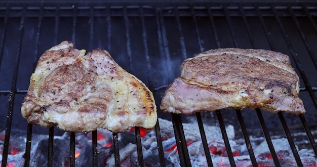 Grilling pork steaks with is fried on fire coals on iron grill