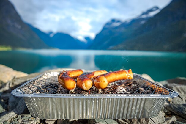 Grilling sausages on disposable barbecue grid. Beautiful Nature Norway natural landscape.