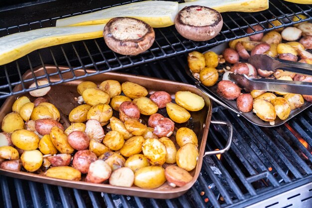 Grilling small potatoes with slices of garlic on an outdoor gas grill.