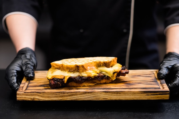 Grillrestaurant. Bijgesneden schot van chef-kok met gerookte runderborst sandwich op houten bord.