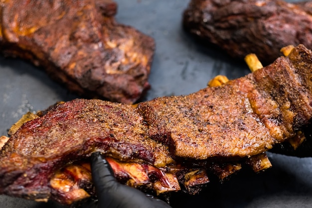 Grillrestaurant keuken. Close-up van gerookte gekruide varkensribbetjes in handen van professionele chef-kok.