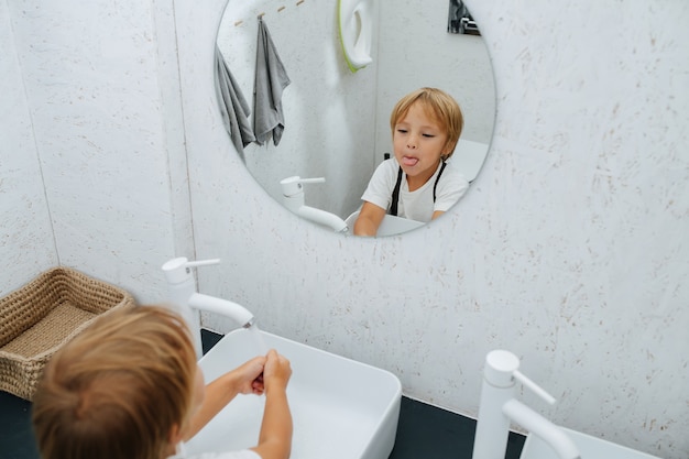 Facendo una smorfia in uno specchio ragazzino che si lava le mani nel lavandino del bagno