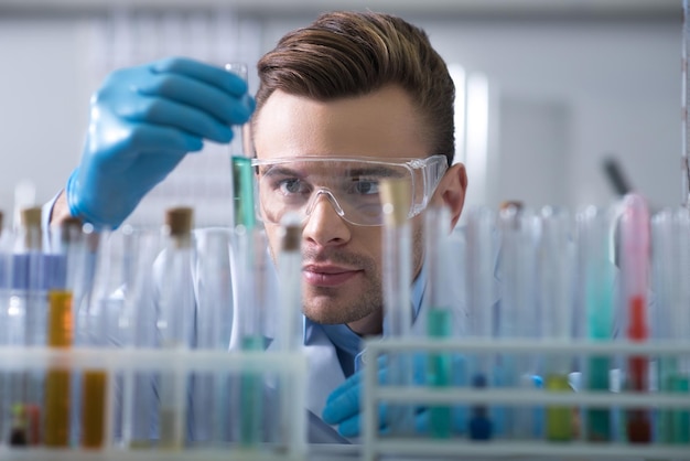 Gripping substance Young interested beardful scientist in a glasses and rubber gloves working in the lab keeping and overlooking test tube