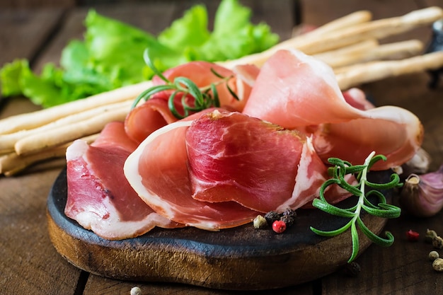 Grissini bread sticks with prosciutto on old wooden background