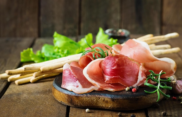 Photo grissini bread sticks with prosciutto on old wooden background