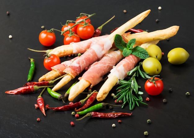 Grissini broodstokken met prosciutto op een zwarte met rozemarijn, peper en olijven