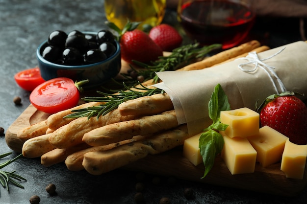 Grissini sticks, snacks and wine on black smokey surface