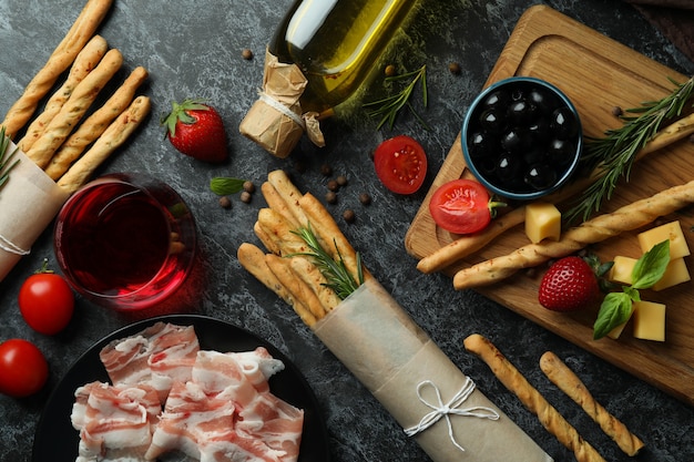 Grissini sticks, snacks and wine on black smokey surface