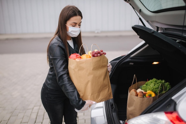 車のトラックのそばの女性の手の中の食料品 保護マスクと使い捨て手袋を着用した女性 エコパケットの新鮮な果物 コロナウイルスCovid19検疫中の食品の買い物