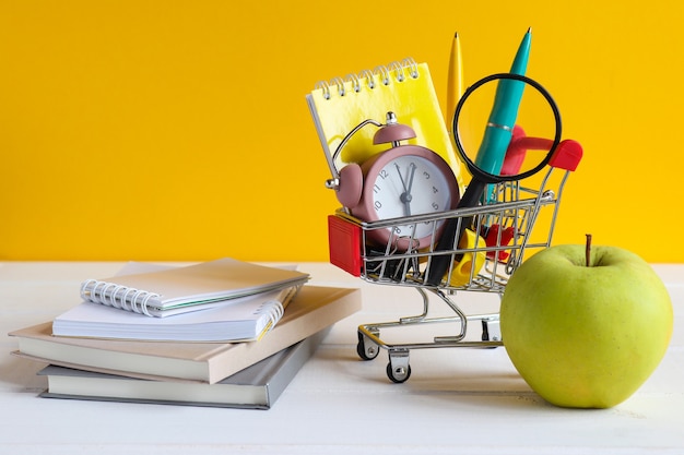 Grocery cart with school supplies green apple note pads and books on the table School shopping