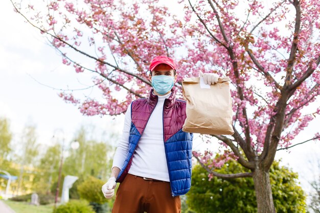 Fattorino della spesa che indossa guanti medici e maschera facciale. shopping online e consegna di generi alimentari, vino e cibo. autoquarantena durante la pandemia di coronavirus. corriere del servizio di consegna cibo