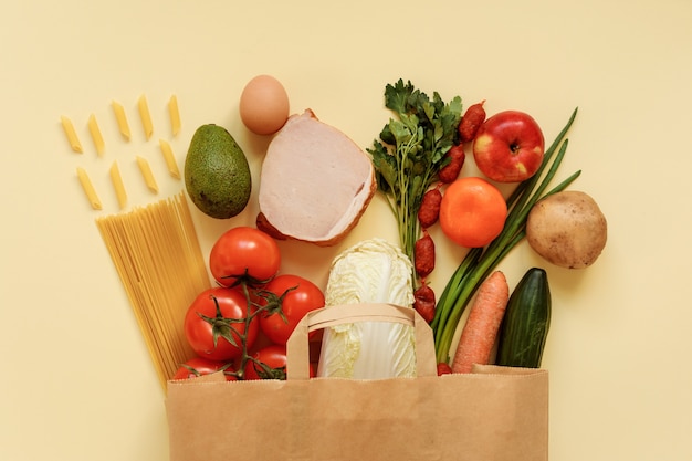 食料品、食品は明るい黄色の背景の紙の買い物袋に詰め込みます。