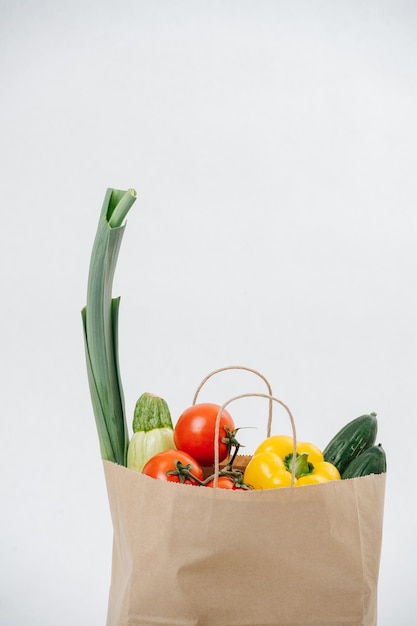 白い背景の上に色とりどりの野菜でいっぱいの食料品の紙袋。