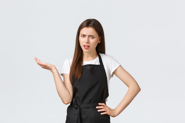 Grocery store employees, small business and coffee shops concept. Annoyed skeptical female barista in black apron saying so what. Saleswoman raise hand in dismay looking bothered