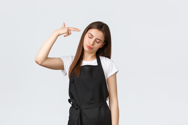 Grocery store employees, small business and coffee shops concept. Annoyed and tired saleswoman in black apron pointing fake gun at head irritated, staring skeptical and bothered.