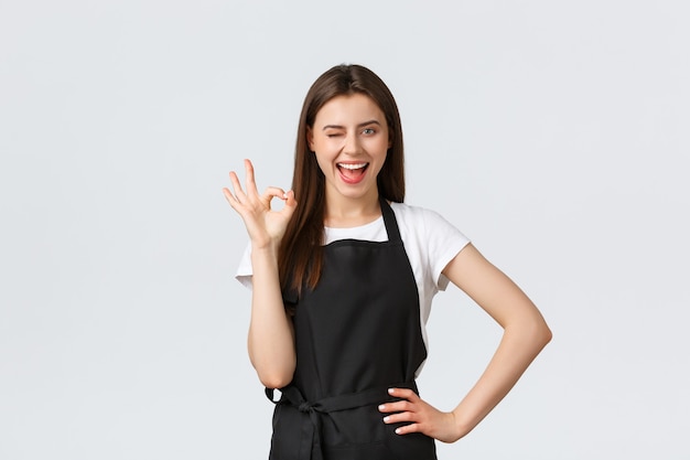 Grocery store employees, small business and coffee shops concept. Cheerful happy smiling barista saying alright, showing okay gesture. Cafe worker guarantee best coffee in town