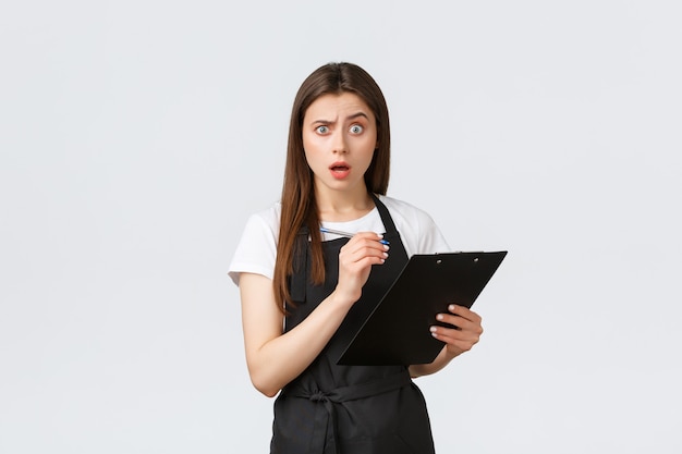 Grocery store employees, small business and coffee shops concept. Confused woman writing on clipboard and stare camera frustrated, having trouble with quantity of items in stock.