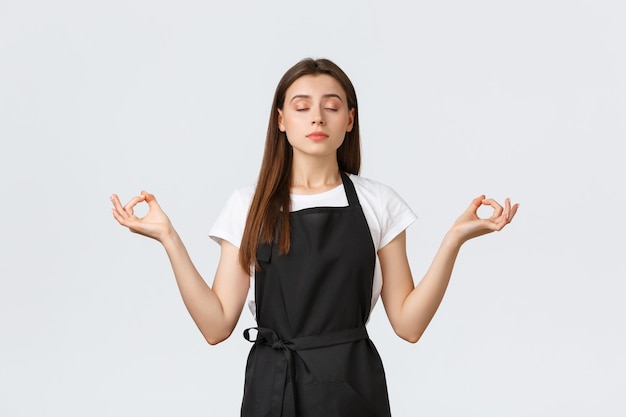 Grocery store employees, small business and coffee shops concept. Cute barista trying stay calm, meditating on break with hands spread sideways, peaceful expression and closed eyes