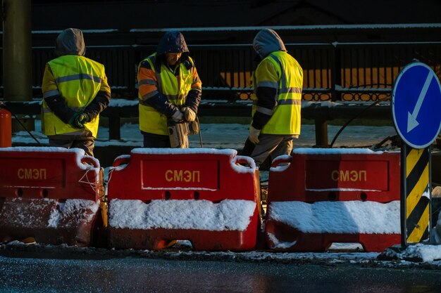 Grodno Belarus January 18 2022 Employees of the road service in special yellow vests perform work on the repair of the roadway Large machinery is working