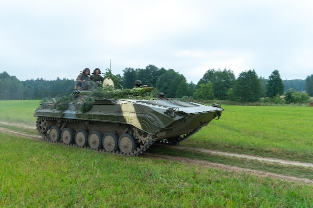 グロドノ ベラルーシ 2020 年 7 月 25 日 歩兵戦闘車は、兵士が搭乗している森を背景に野原に沿った未舗装の道路に乗ります 演習でのさまざまな軍事装備