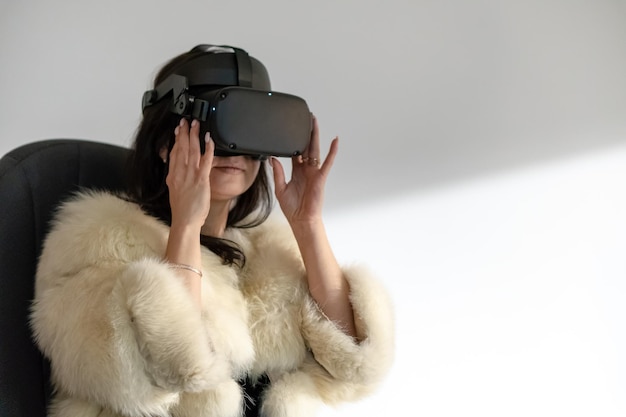 Grodno belarus june 012020 young girl in a fashionable white\
fur coat wearing virtual reality glasses using vr technologies in\
everyday life introduction of augmented reality in life