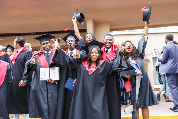 Grodno belarus june 2018 happy foreign african medical students\
in square academic graduation caps and black raincoats during\
commencement with diploms after finishing studies