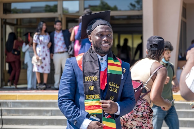 Grodno belarus june 2021 happy foreign african medical students\
in square academic graduation caps and black raincoats during\
commencement with diploms after finishing studies