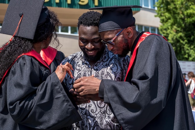Grodno belarus june 2021 happy foreign african medical students\
in square academic graduation caps and black raincoats during\
commencement with diploms after finishing studies
