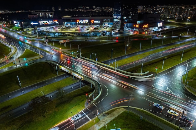 Grodno belarus november 2021 night time on roundabout on road\
with cars with headlights on highway and light in windows of\
multistory buildings life in big city looking down on traffic